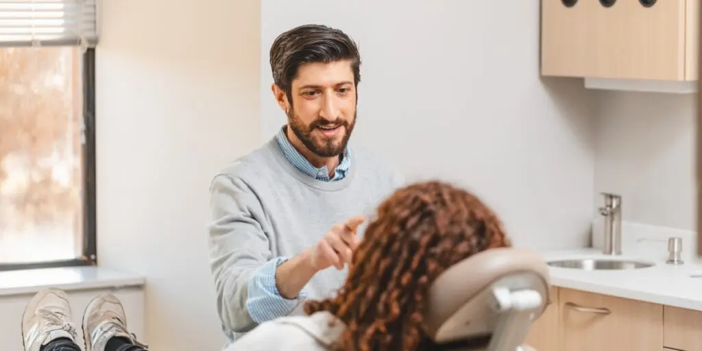 Clinician explains treatment to a patient seated in a dental chair in a bright clinic.